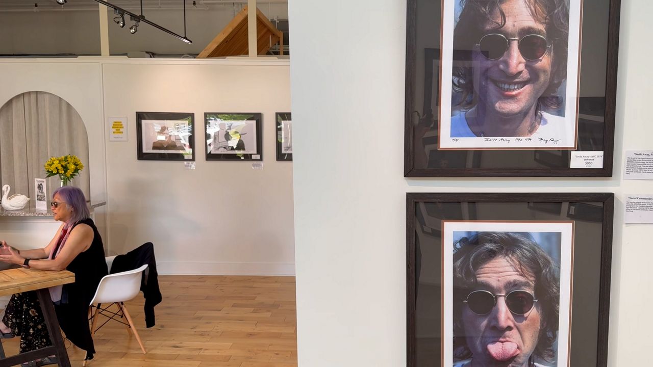 Candid photos of John Lennon hang in Cygnet gallery as Pang speaks with visitors. (Spectrum News/David Ledford)