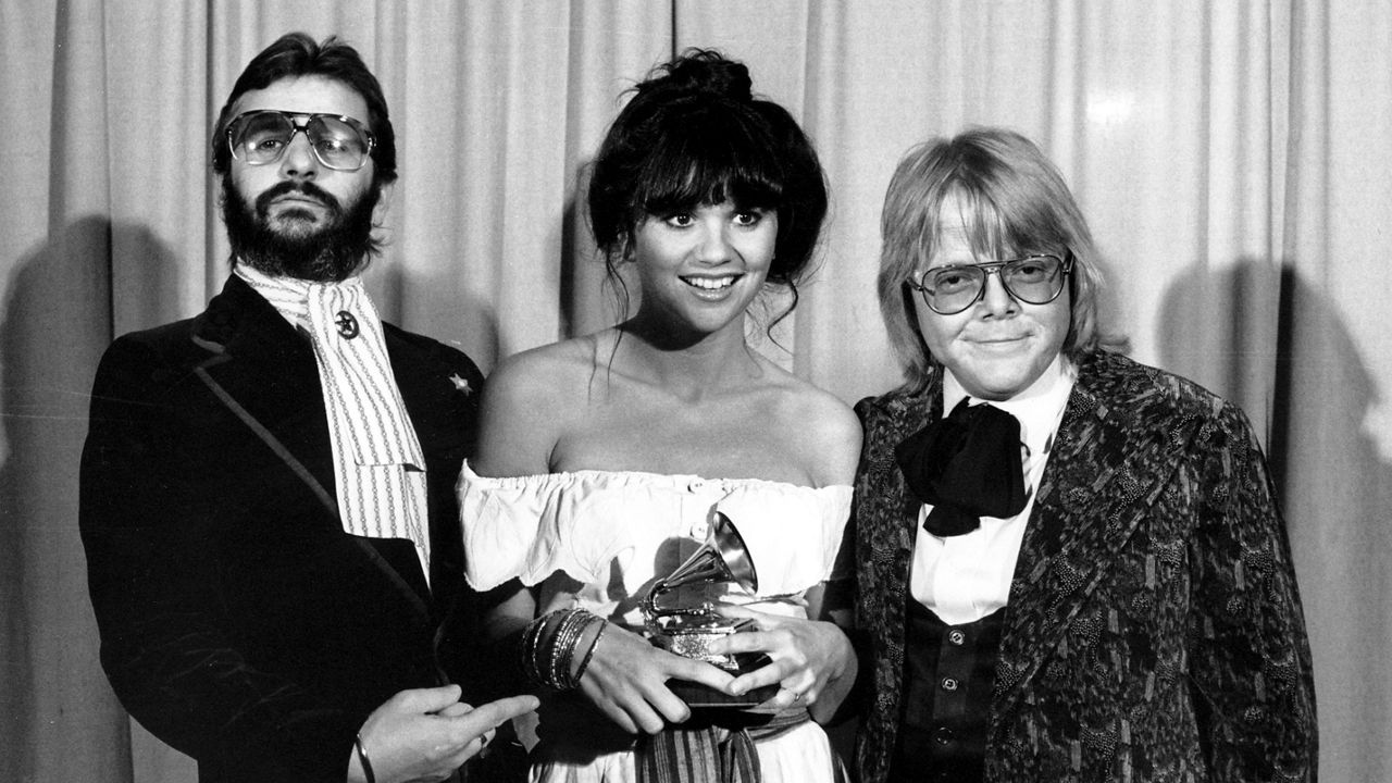 This Feb. 20, 1977, file photo shows singer Linda Ronstadt is flanked by Ringo Starr, left, and Paul Williams after she was named best pop singer for her "Hasten Down the Wind" at The 19th Annual Grammy Awards in Los Angeles. (AP Photo)