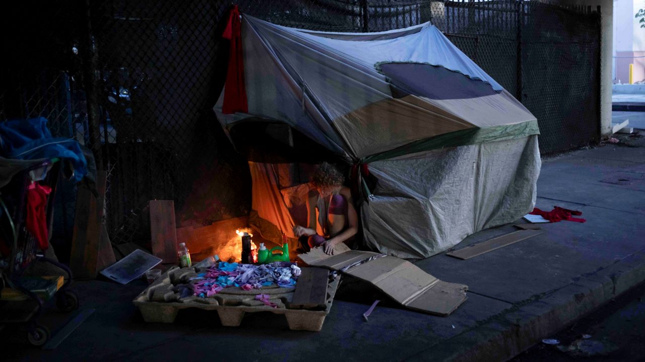 A homeless woman ignites a fire using cardboard beneath the section of Interstate 10 that has been closed due to a recent fire in Los Angeles, Tuesday, Nov. 14, 2023. (AP Photo/Jae C. Hong)