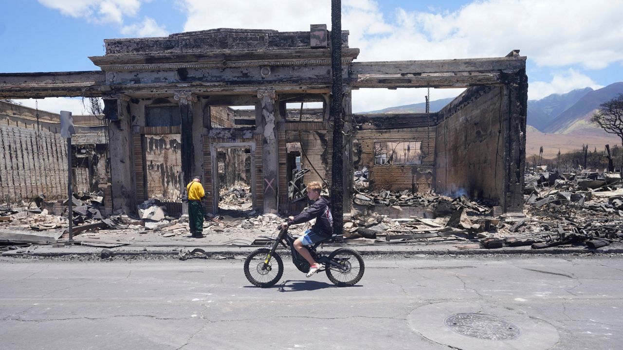 A boy rides along Main Street past wildfire damage on Friday, Aug. 11, 2023, in Lahaina, Hawaii. (AP Photo/Rick Bowmer)