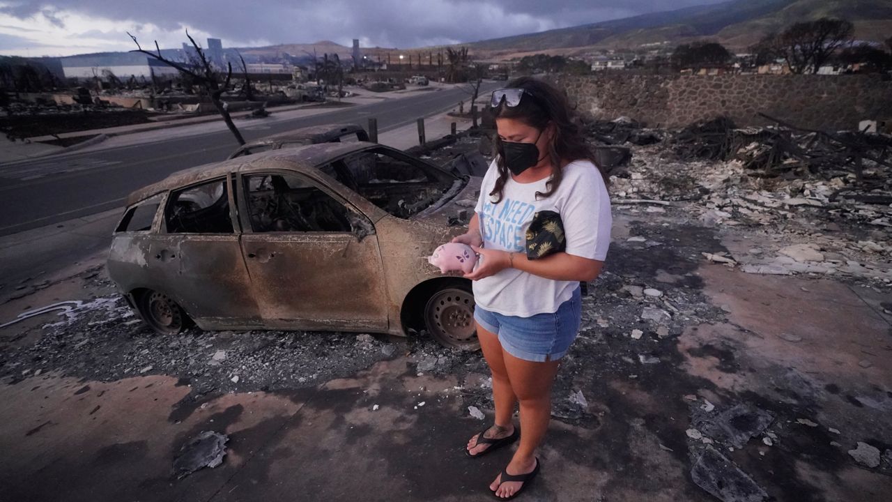 Summer Gerling picks up her piggy bank found in the rubble of her home following the wildfire on Aug. 10, 2023, in Lahaina, Hawaii. Lahaina residents are grappling with a range of feelings as Maui authorities plan to begin allowing them back into what has become known as the "burn zone." (AP Photo/Rick Bowmer, File)