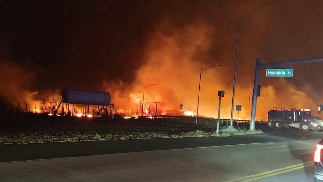 This photo provided by County of Maui shows fire and smoke filling the sky from wildfires on the intersection at Hokiokio Place and Lahaina Bypass in Maui, Hawaii on Tuesday, Aug. 8, 2023. Wildfires in Hawaii fanned by strong winds burned multiple structures in areas including historic Lahaina town, forcing evacuations and closing schools in several communities Wednesday, and rescuers pulled a dozen people escaping smoke and flames from the ocean. (Zeke Kalua/County of Maui via AP)