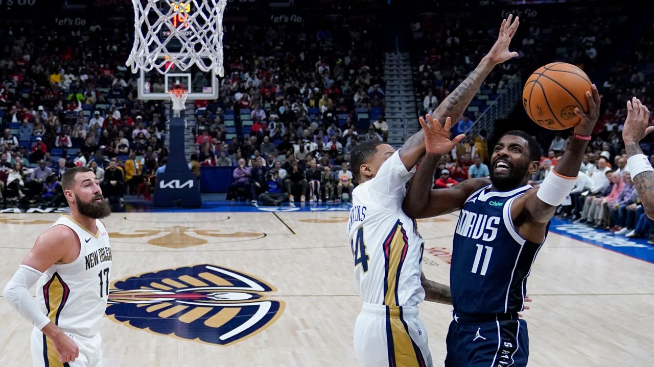 Dallas Mavericks guard Kyrie Irving (11) drives to the basket against New Orleans Pelicans guard Jordan Hawkins (24) and center Jonas Valanciunas (17) in the first half of an NBA basketball game in New Orleans, Sunday, Nov. 12, 2023. (AP Photo/Gerald Herbert)