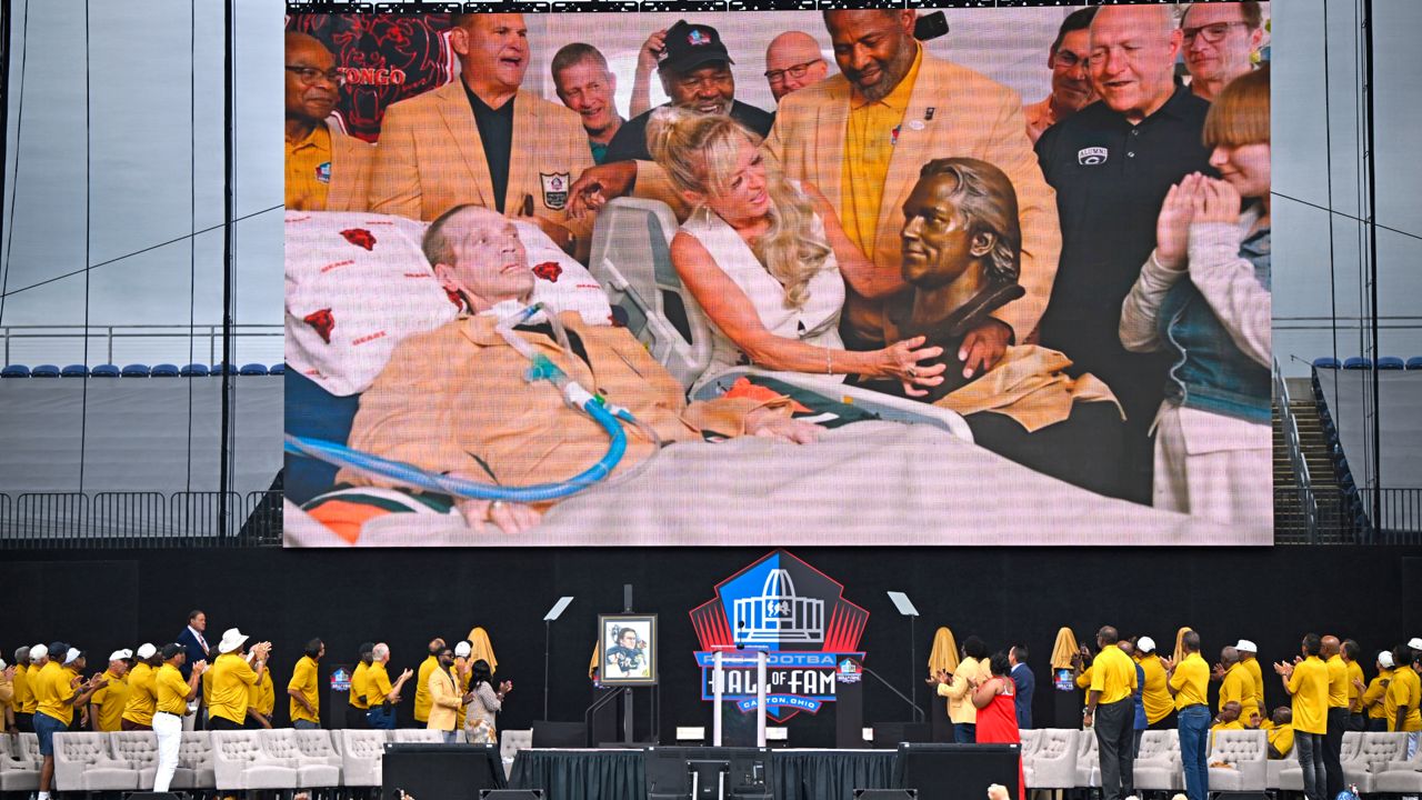 Misty McMichael, wife of former NFL player Steve McMichael, left, unveils his bust during an induction ceremony from their home, on the video screen at the Pro Football Hall of Fame, in Canton, Ohio, Saturday, Aug. 3, 2024. 