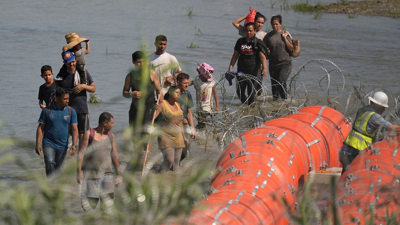 Migrants trying to enter the U.S. from Mexico approach the site where workers are assembling large buoys to be used as a border barrier along the banks of the Rio Grande in Eagle Pass, Texas, Tuesday, July 11, 2023. (AP Photo/Eric Gay)