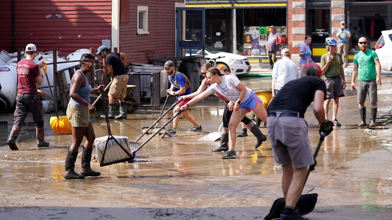 Volunteers clean up a downtown parking area on the banks of the Winooski River, Wednesday, July 12, 2023, in Montpelier, Vt. Following a storm that dumped nearly two months of rain in two days, Vermonters are cleaning up from the deluge of water. (AP Photo/Charles Krupa)