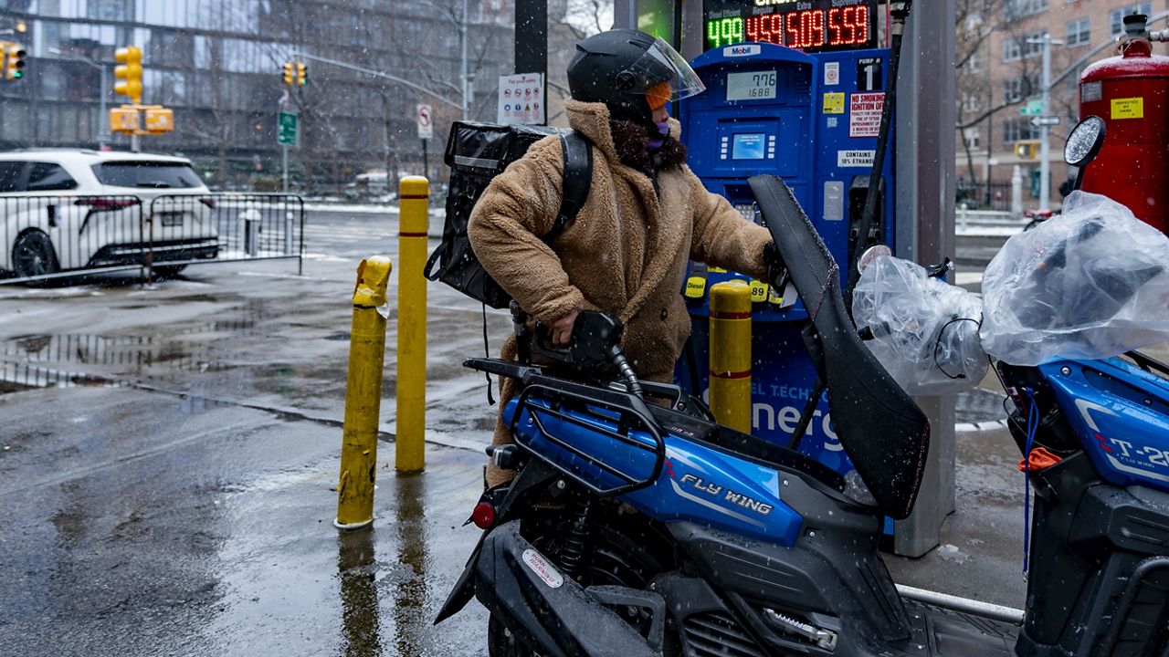 A man dispenses gasoline into a moped at a Mobil station on Friday, Jan. 19, 2024, in New York. (AP Photo/Peter K. Afriyie)