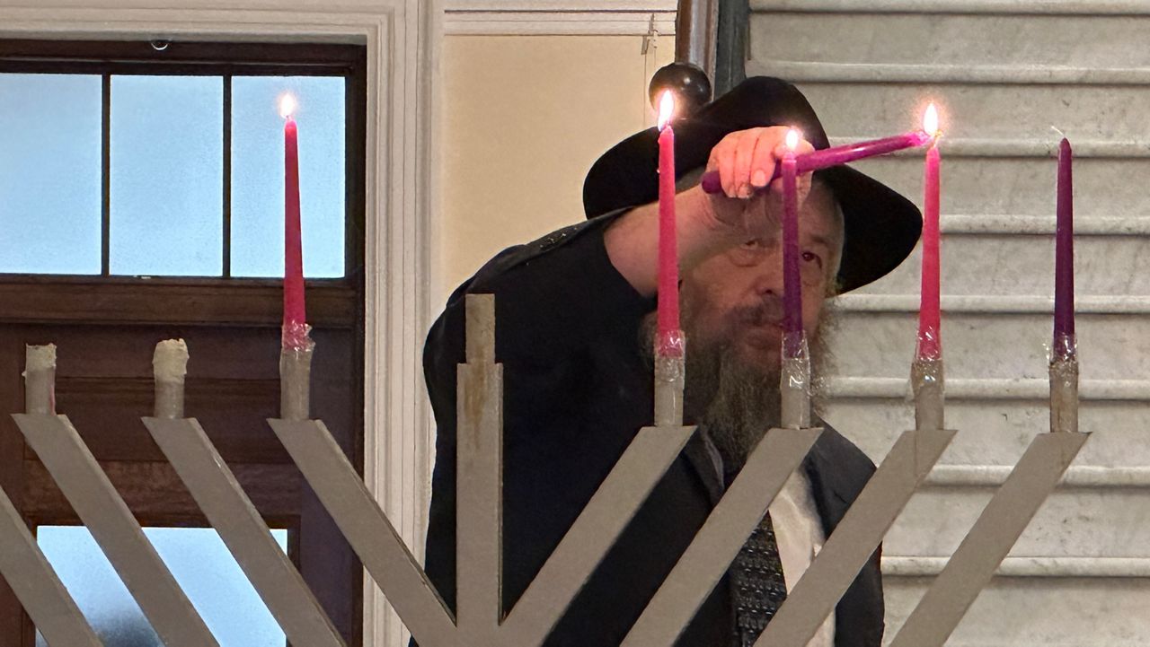 Rabbi Moshe Wilansky lights the menorah Monday at the State House. (Spectrum News/Susan Cover)