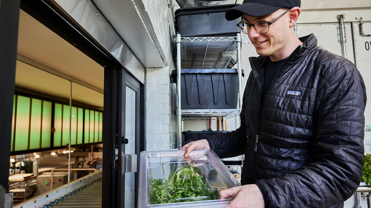 St. Louis native and Neon Greens owner Josh Smith puts greens on the conveyor belt at his new restaurant that opened Tuesday, March 19. (Photo by Izaiah Johnson)