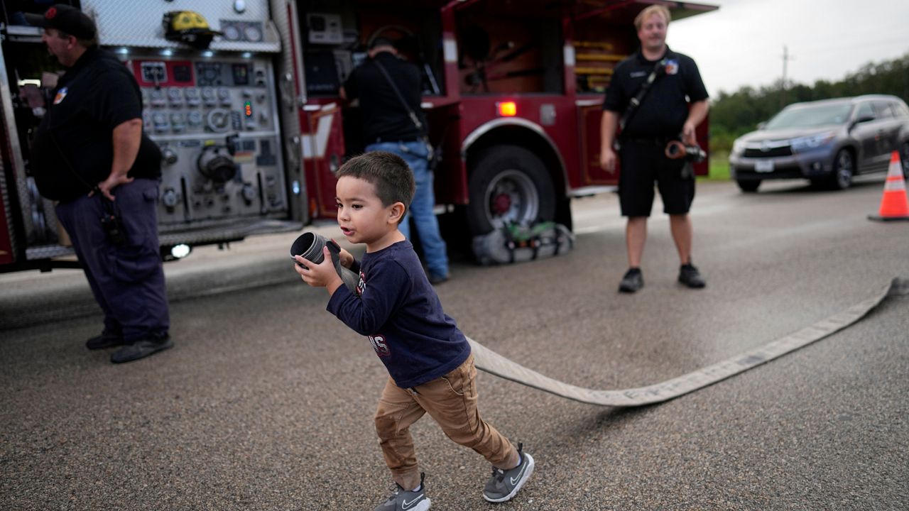 Noah Hernandez, 3, carries a fire hose while attending a National Night Out event with his parents in the Colony Ridge development Tuesday, Oct. 3, 2023, in Cleveland, Texas. The booming Texas neighborhood is fighting back after Republican leaders took up unsubstantiated claims that it has become a magnet for immigrants living in the U.S. illegally and that cartels control pockets of the neighborhood. (AP Photo/David J. Phillip)