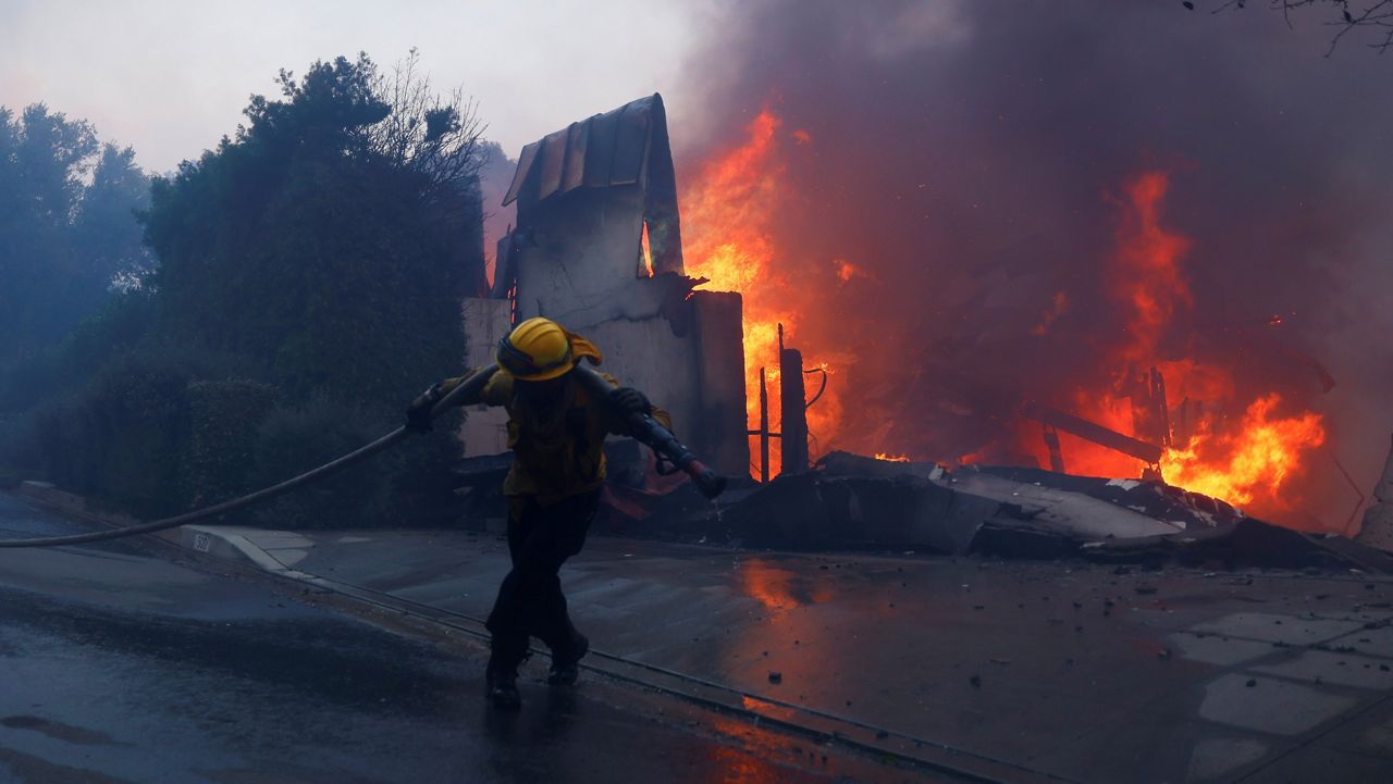 A firefighter battles the advancing Palisades Fire as it burns a structure in the Pacific Palisades neighborhood of Los Angeles on Tuesday. (AP Photo/Etienne Laurent)