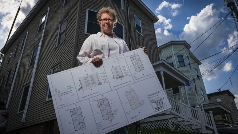 Amy Smith, founder of Healthy Home Works, stands in front of a triple-decker building in Lewiston's Tree Streets neighborhood on Wednesday, which her organization is transforming into affordable condos for first-time home buyers. Smith holds floor plans for the spacious units. Credit: Troy R. Bennett / BDN