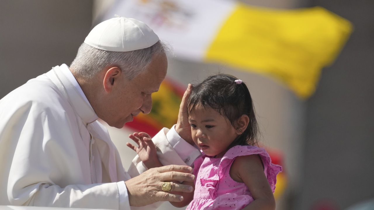 Pope Leo XIV caresses a little girl as he arrives to celebrate a Mass for the Jubilee of New Religious Associations on Pentecost Day in St. Peter's Square at the Vatican, Sunday, June 8, 2025. (AP Photo/Andrew Medichini)