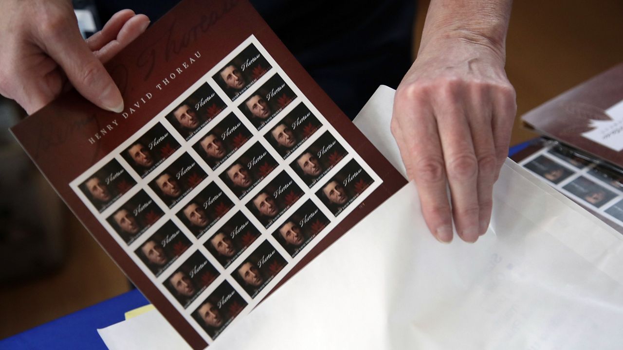 In this May 23, 2017 photo, U.S. Postal Service worker Dianne Zambelli places a sleeve of newly dedicated Henry David Thoreau postage stamps for purchase in a bag at Walden Pond in Concord, Mass. (AP Photo/Elise Amendola)