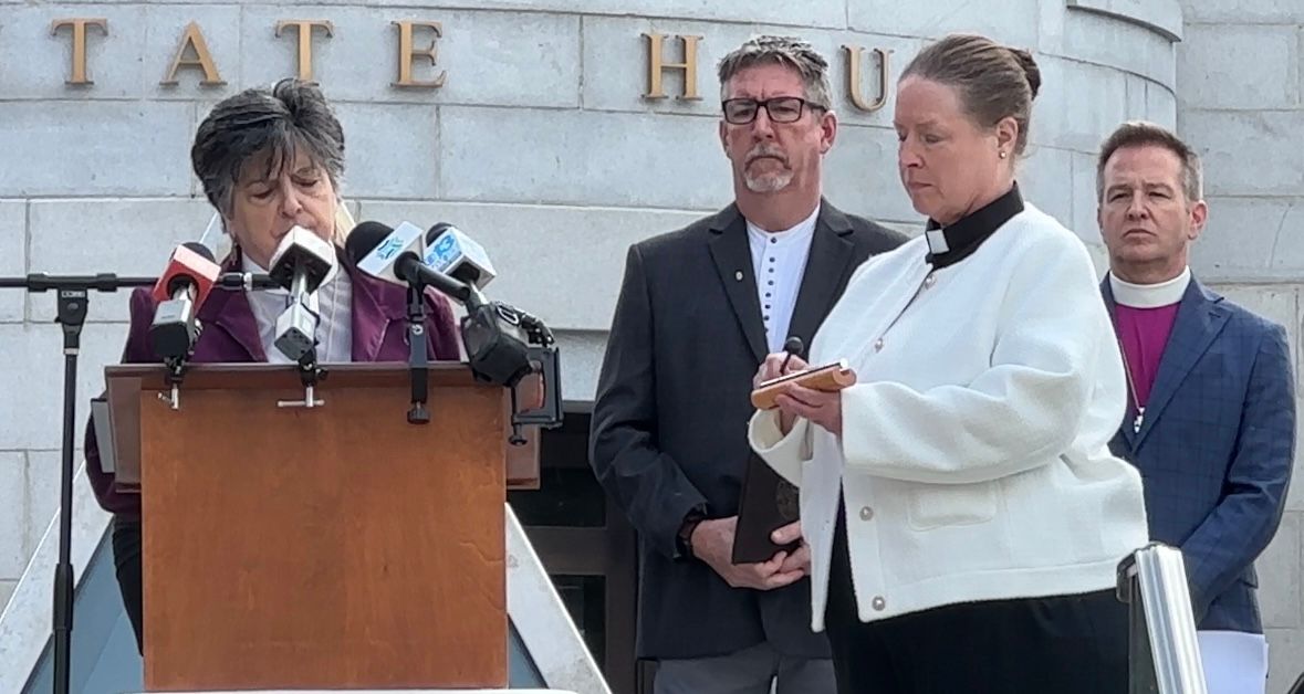 The Rev. Marisa Laviola reads the names of the Lewiston shooting victims while the Rev. Jane field taps a bell during a Tuesday service to remember the Oct. 25 tragedy at the State House. (Spectrum News/Susan Cover)