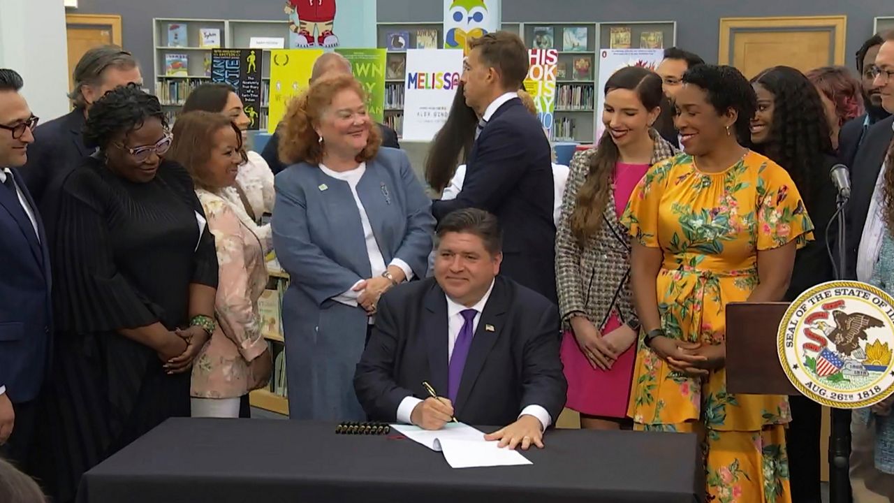 In this screenshot from a livestream broadcast by the State of Illinois, Gov. J.B. Pritzker signs a bill, Monday, June 12, 2023, at Harold Washington Library's Thomas Hughes Children's Library in downtown Chicago. The new law will require the state's libraries to uphold a pledge not to ban material because of partisan disapproval, starting on Jan. 1, 2024. If they refuse, they will not receive state funding. Pritzker said the law will make Illinois the first state in the nation to outlaw book bans. (State of Illinois via AP)