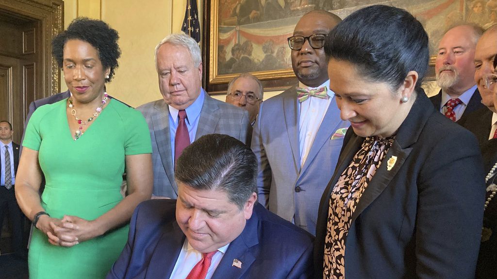 With Illinois state Comptroller Susana Mendoza, right, looking on, Gov. J.B. Pritzker signs a law at the state Capitol in Springfield on Wednesday, May 10, 2023 which provides full disability benefits for Chicago first responders who suffer from COVID-19 contracted on the job before vaccines were available. Mendoza's brother, police Det. Joaquin Mendoza, was denied benefits because he could not show the moment on the job that he contracted the disease. He suffers from long COVID that resulted in five strokes and the loss of both kidneys. (AP Photo/John O'Connor)