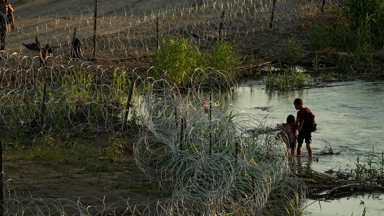 A Texas state trooper watches as young migrants walk along concertina wire on the banks of the Rio Grande as they try to enter the U.S. from Mexico in Eagle Pass, Texas, Thursday, July 6, 2023. (AP Photo/Eric Gay)