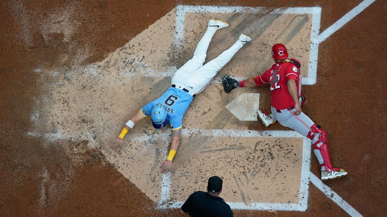 Milwaukee Brewers' Jake Bauers (9) slides safely past the tag of Cincinnati Reds' Luke Maile during the second inning of a baseball game, Friday, Aug. 9, 2024, in Milwaukee.