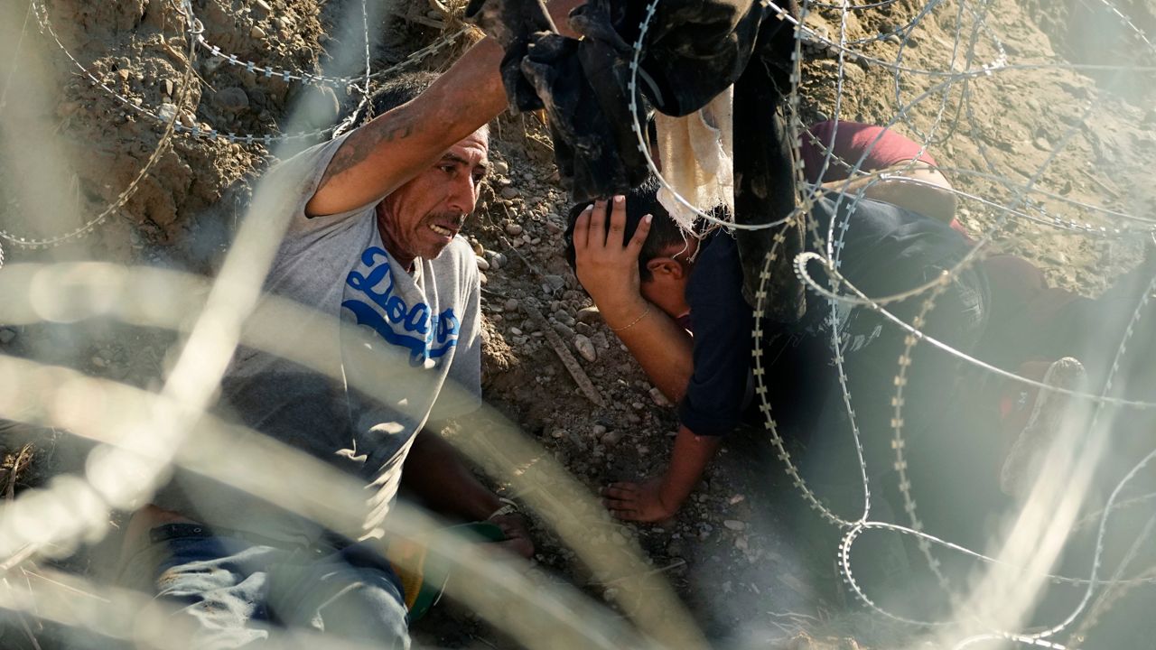 Migrants who crossed the Rio Grande from Mexico to the U.S. work their way through concertina wire, Friday, Sept. 22, 2023, in Eagle Pass, Texas. (AP Photo/Eric Gay)