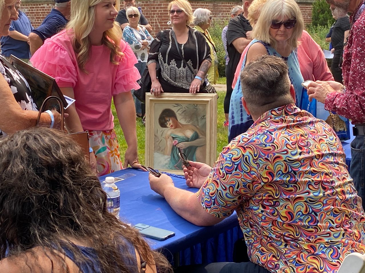 people gathered at tables, with one woman holding a painting