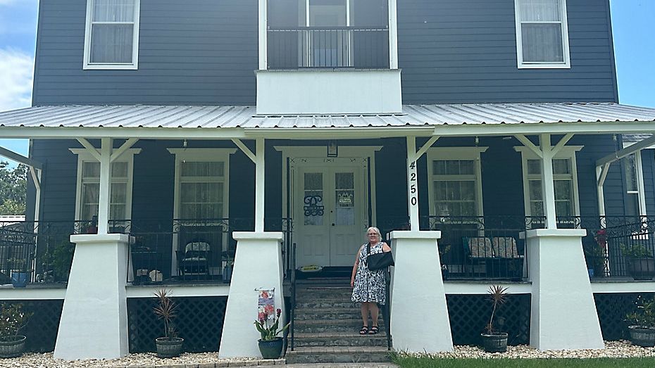 Rebecca Burke stands in a front of the home where she has lived for nearly 30 years. The building may be destroyed if a proposed freeway to connect State Road 417 to the Orlando Sanford International Airport is approved. (Spectrum News/Brandon Spencer)