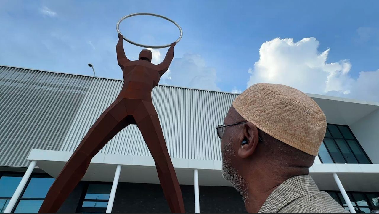 Abdul Karim Ali looks up at the statue created in honor of his late father, Joseph E. Savage. (Spectrum Bay News 9)
