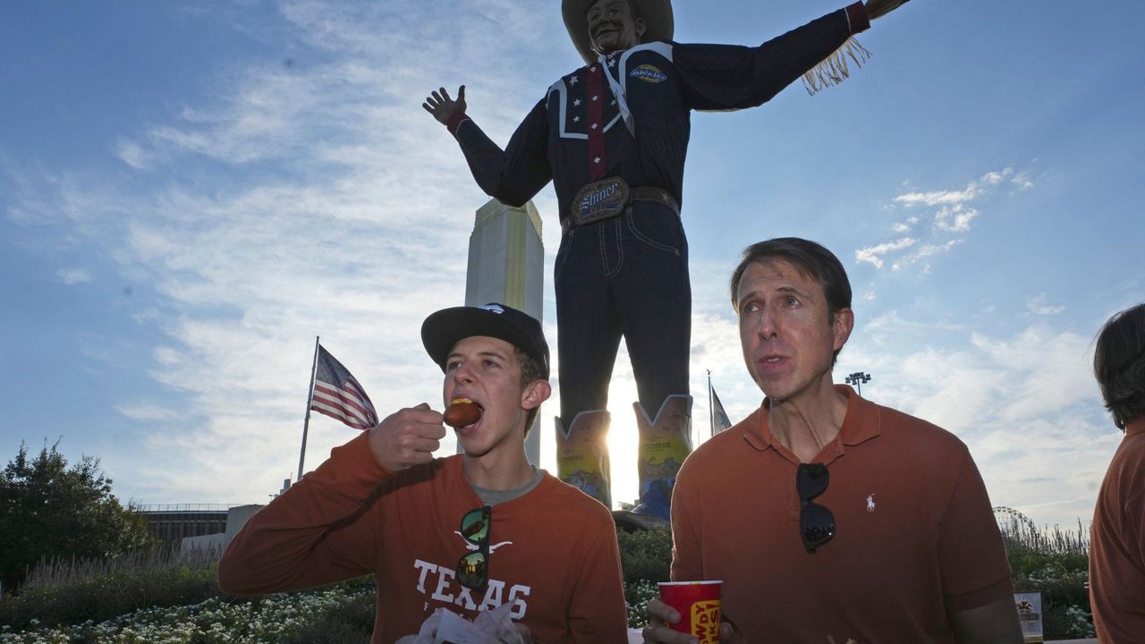 Dennis McGinnis, left, eats a hot corn dog breakfast with his dad Davin McGinnis in front of Big Tex before heading to see an NCAA college football game between Oklahoma and Texas at the Cotton Bowl in Dallas, Saturday, Oct. 7, 2023. (AP Photo/LM Otero)