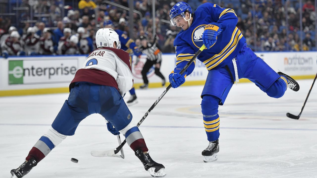 buffalo sabres player follows through on a shot, defended by colorado avalanche player