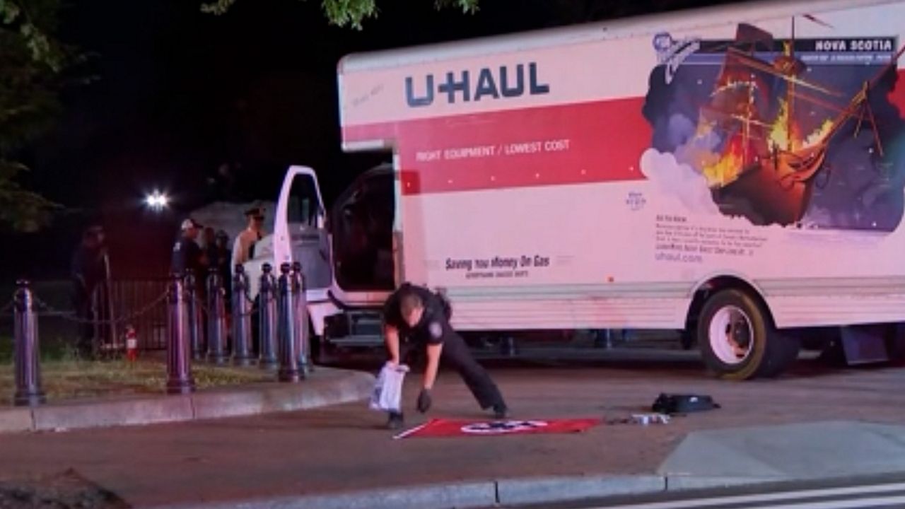 An officer picks up a Nazi flag after authorities said that Sai Varshith Kandula, 19, of Chesterfield, Missouri, intentionally crashed a U-Haul truck into a security barrier at a park across from the White House. (Photo courtesy of CNN) 