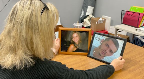 Keli Clark sits at a table looking two framed pictures, one of her late daughter and the other of her late son. 