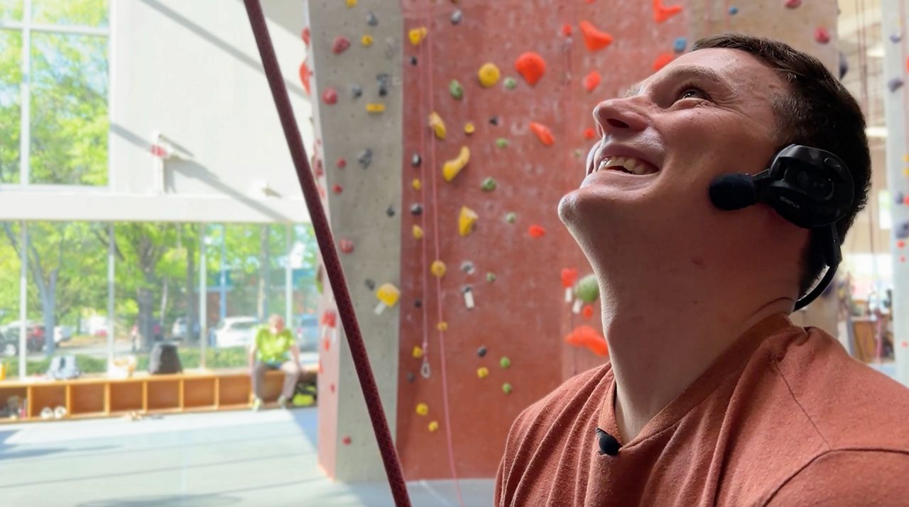 David Crye smiles while Leah Grosjean successfully completes a route while training. (Spectrum News 1/Rachel Boyd)