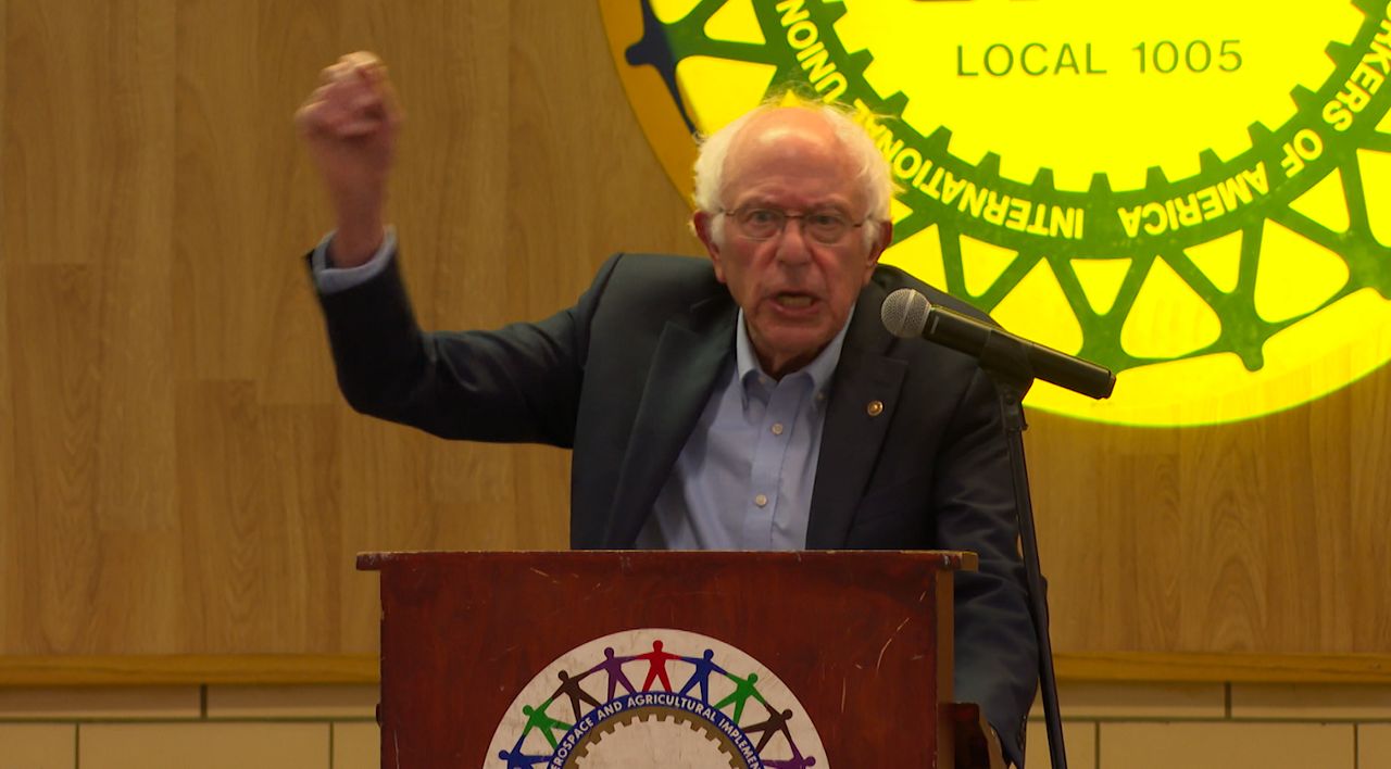 Bernie Sanders raises his hand as he speaks at a podium in Parma. 