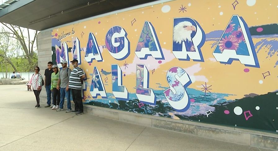 Tourists take a photo in front of a Niagara Falls mural. (Spectrum News 1/Brianne Roesser Photo)