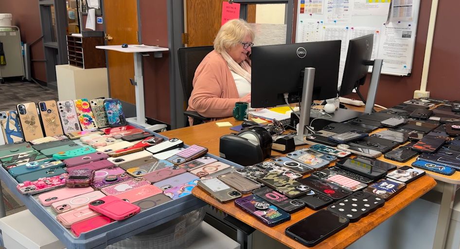 A school employee sits with phones scattered on her desk 