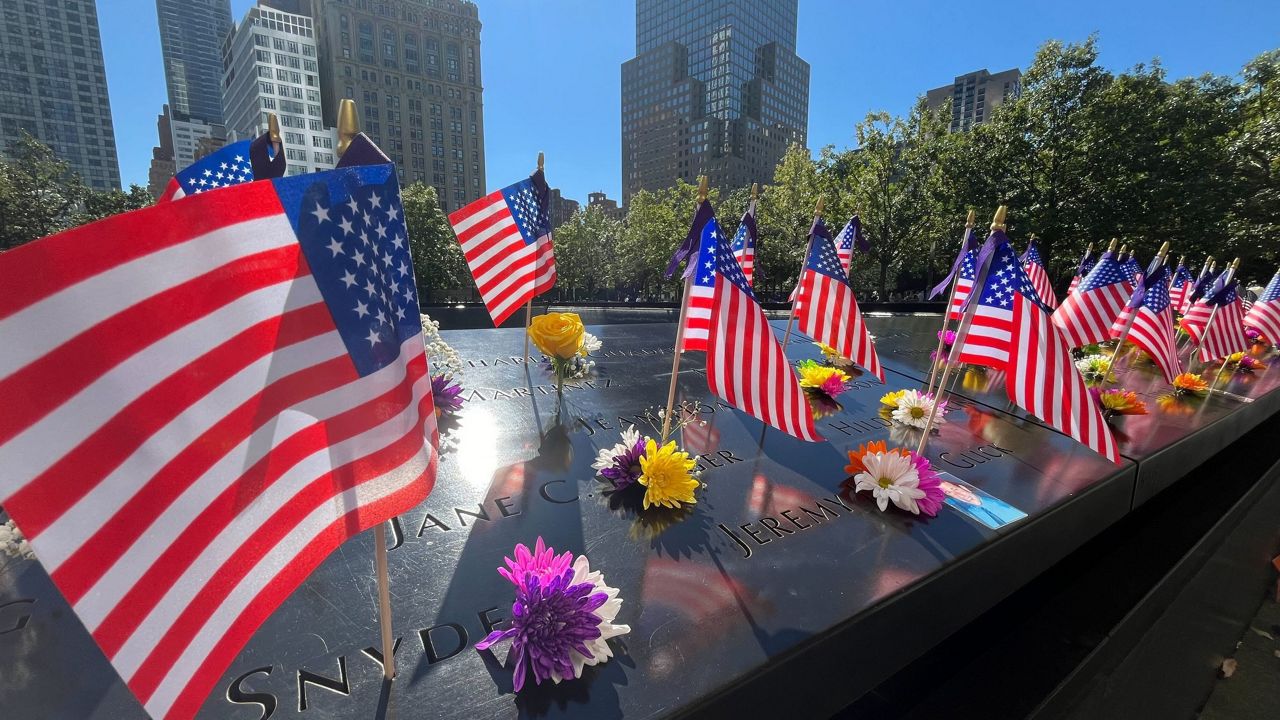 Flags and flowers are placed by the names of those killed during the Sept. 11, 2001, attacks at the reflecting pools at the National September 11 Memorial & Museum, Tuesday, Sept. 10, 2024, in New York. (AP Photo/Donald King)