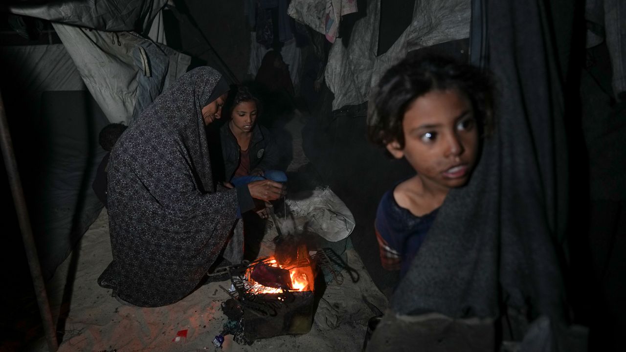 Shireen Daifallah, who was displaced with her children from northern Gaza, checks the fire next to their tent at a camp for displaced people in Deir al-Balah. Gaza Strip, Saturday, Nov. 30, 2024. (AP Photo/Abdel Kareem Hana)