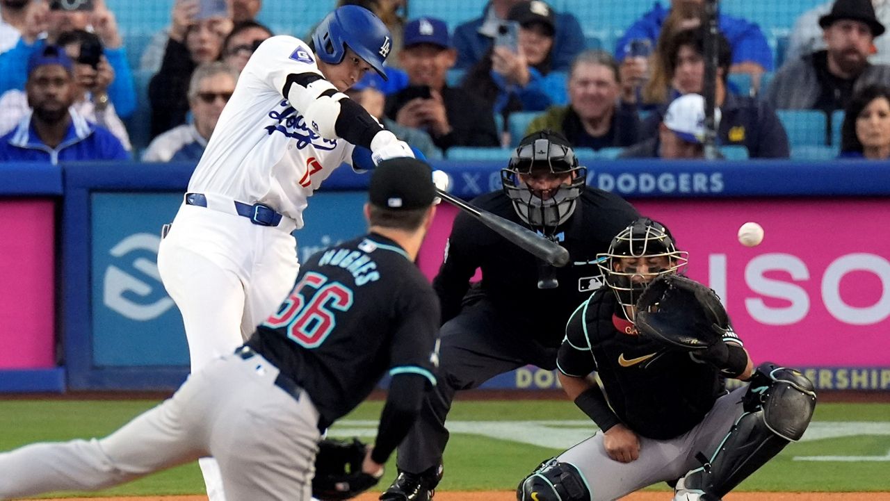 Los Angeles Dodgers' Shohei Ohtani, left, hits a single as Arizona Diamondbacks starting pitcher Brandon Hughes, second from left, and catcher Gabriel Moreno, right, watch along with home plate umpire Chad Fairchild during the first inning of a baseball game Wednesday, May 22, 2024, in Los Angeles. (AP Photo/Mark J. Terrill)