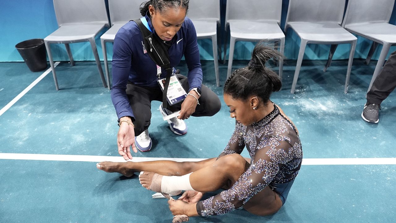 Simone Biles of the United States has her ankle taped after competing on the uneven bars during a women's artistic gymnastics qualification round at Bercy Arena at the 2024 Summer Olympics, Sunday, July 28, 2024, in Paris, France. (AP Photo/Charlie Riedel)