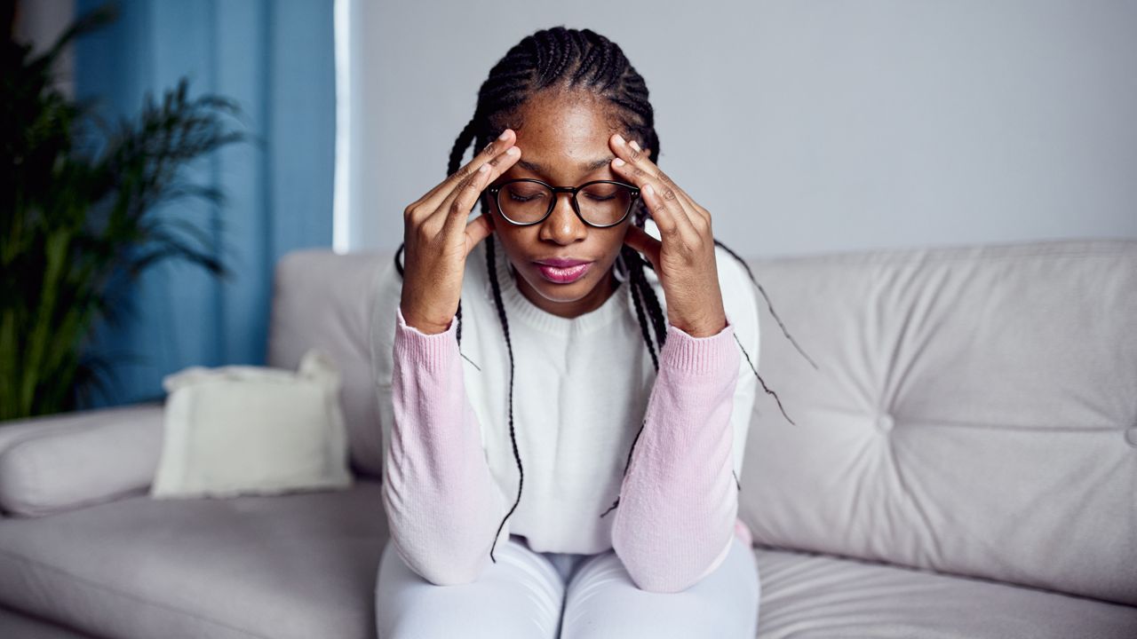 A young woman is sitting on the sofa at home with her head in her hands. The concept of health problems , headache or stress. (Getty)