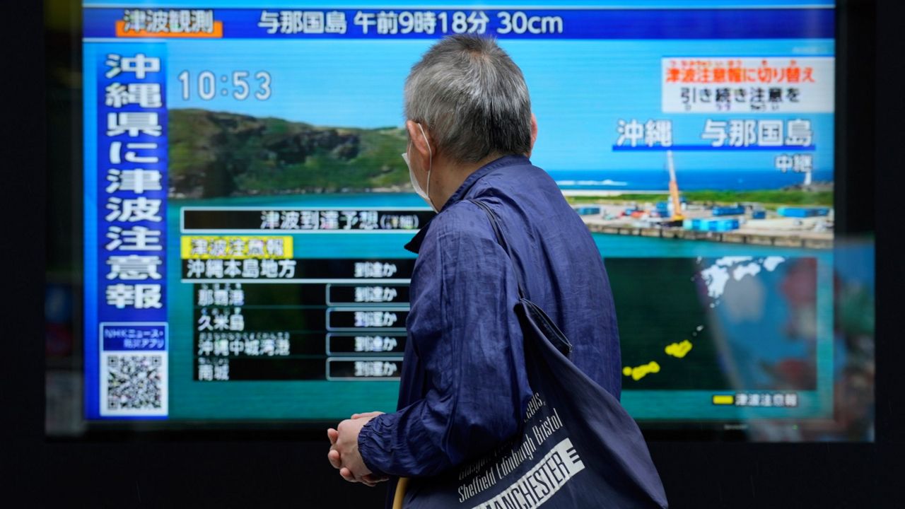 A person stands along a sidewalk to watch a TV showing a breaking news on tsunami for Okinawa region Wednesday, April 3, 2024, in Tokyo. Japan issued tsunami alerts Wednesday after a strong quakes near Taiwan. (AP Photo/Eugene Hoshiko)