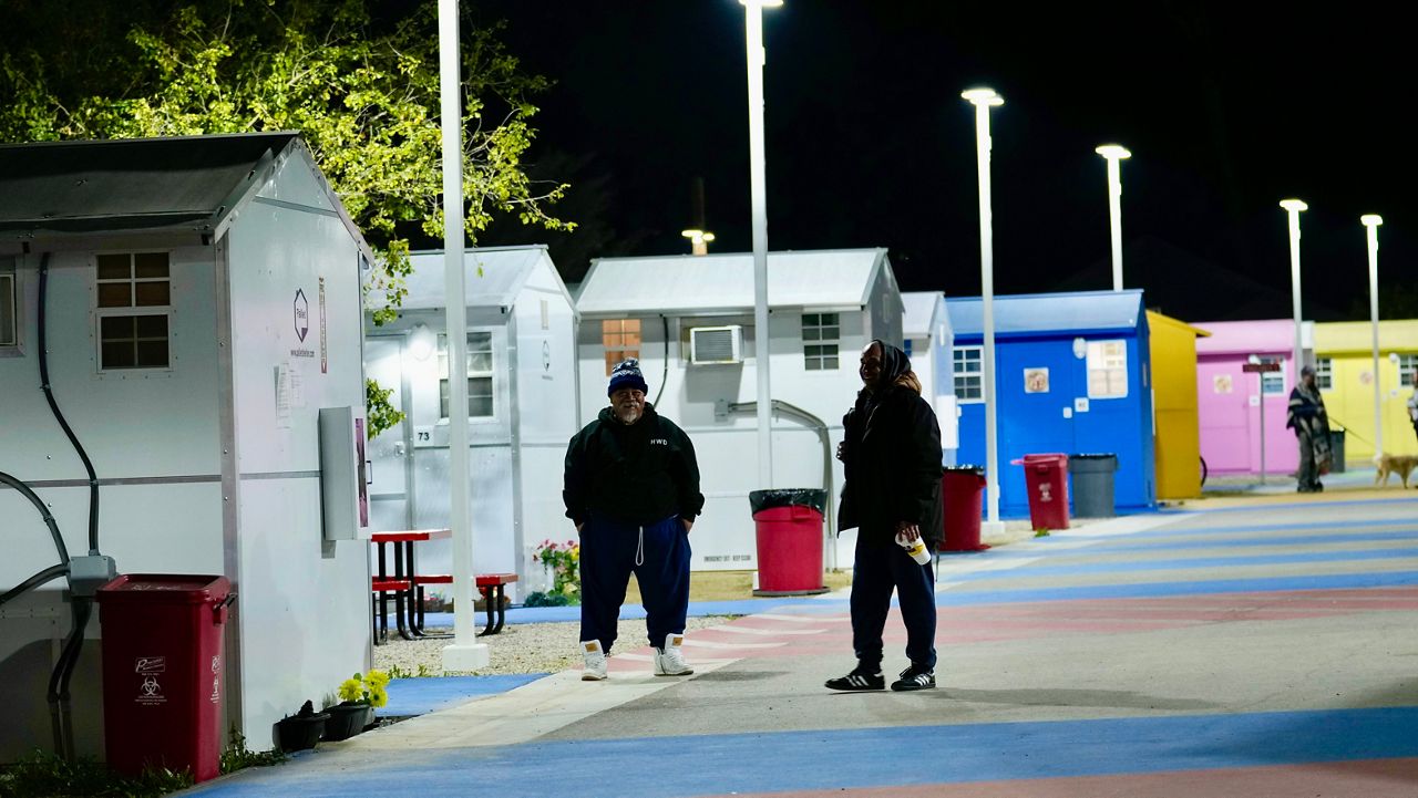 Two residents of a tiny homes community, built for the homeless, stand outside a row of the units. (AP Photo/Marcio Jose Sanchez)