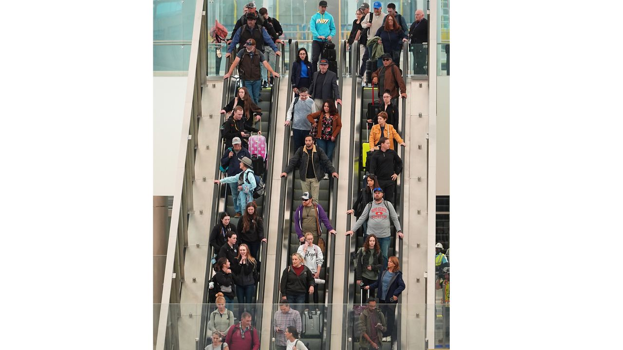 Travellers head down an escalator after clearing through a security checkpoint in Denver International Airport Friday, Nov. 7, 2025, in Denver. (AP Photo/David Zalubowski)
