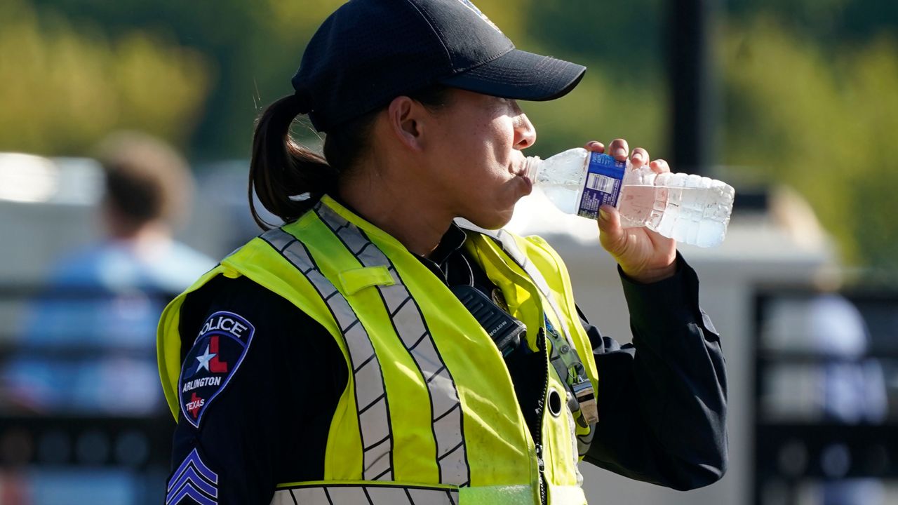 A police officer directing traffic takes a break to drink water after a sporting event in Arlington, Texas, Saturday, Aug. 19, 2023. The summer of 2023 may be drawing to a close — but the extreme heat is not: More record-shattering temperatures — this time across Texas — are expected Saturday and Sunday as the U.S. continues to bake. (AP Photo/LM Otero)