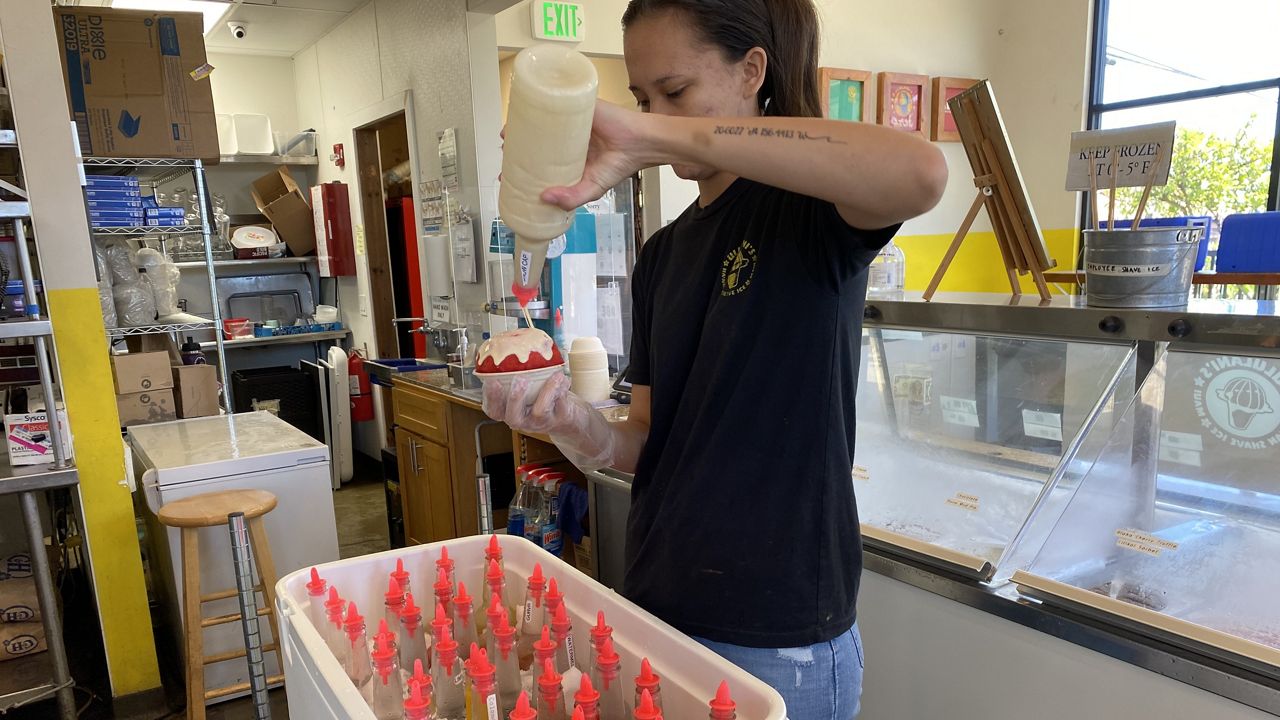 Tiare Arista, an employee at Ululani's Shave Ice in Wailuku, adds the "snow cap" to a strawberry-flavored shave ice. (Michelle Broder Van Dyke/Spectrum News)