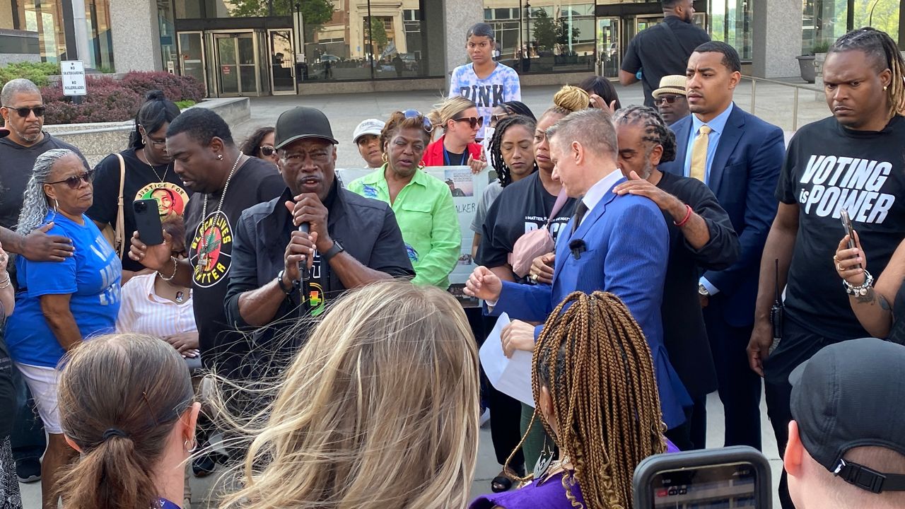 man in black ball cap speaks with man in blue jacket in the center of a crowd