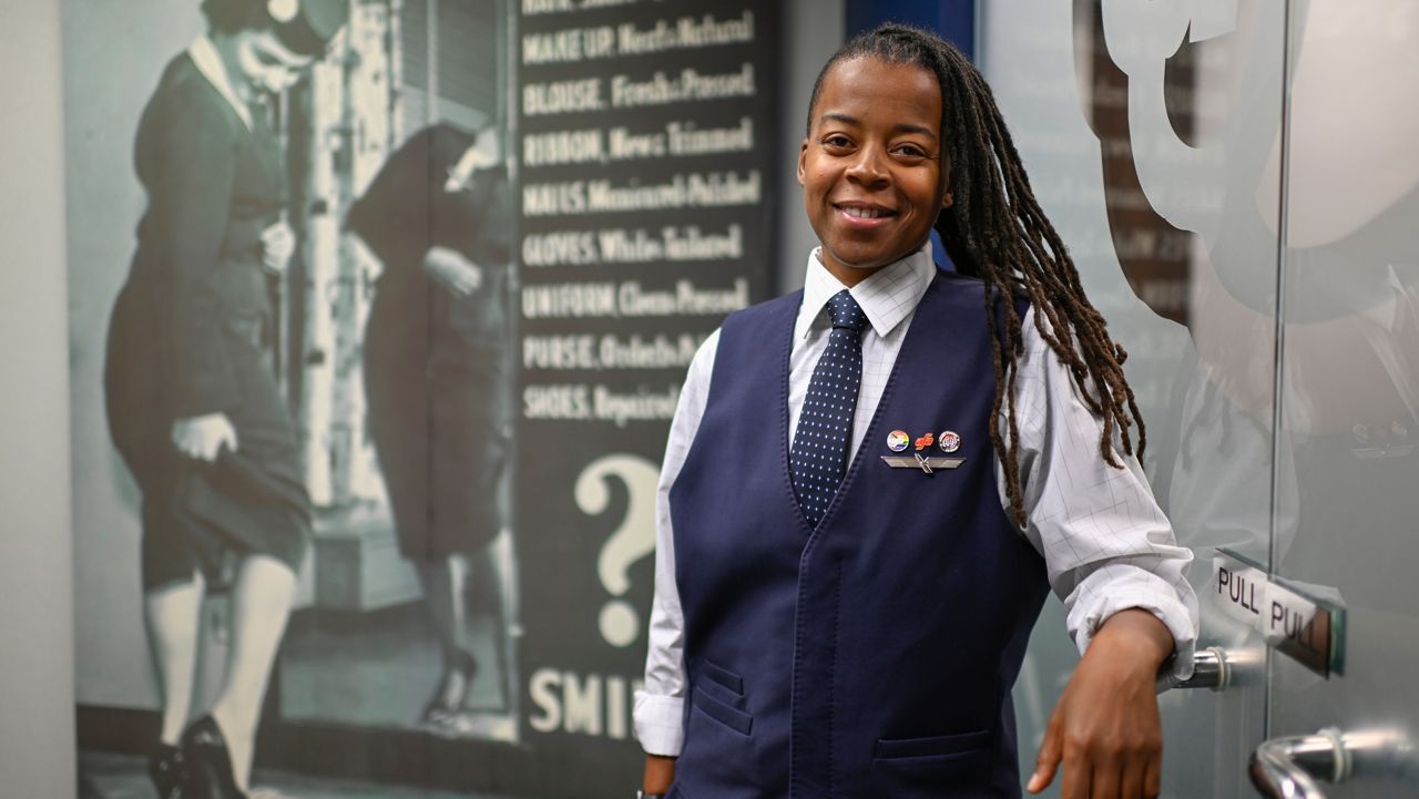 Keturah Johnson, international vice president for flight attendant union AFA-CWA, poses by a decades old, outdated poster with rules and uniforms for flight attendants, at her headquarters office, Wednesday, Sept. 18, 2024, in Washington. (AP Photo/John McDonnell)