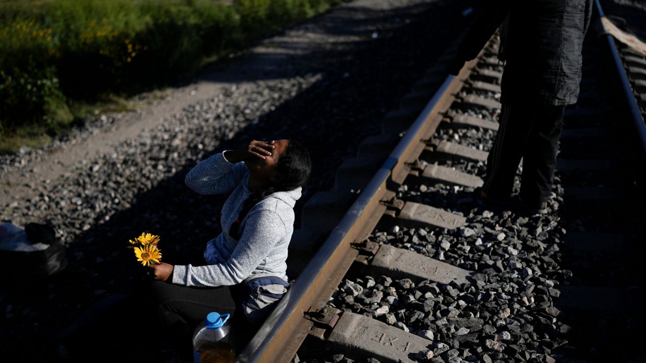 A Venezuelan migrant laughs as she jokes with her husband, who gave her a few flowers he picked in the grass, as they wait along the rail lines in hopes of boarding a freight train heading north in Huehuetoca, Mexico, Wednesday, Sept. 20, 2023. (AP Photo/Eduardo Verdugo)