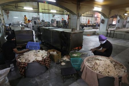 A cook in a Sikh kitchen cooking in an extremely large pot.