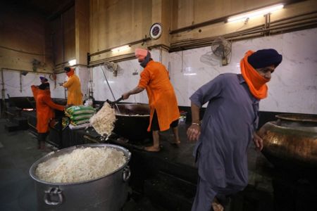 A cook in a Sikh kitchen cooking in an extremely large pot.